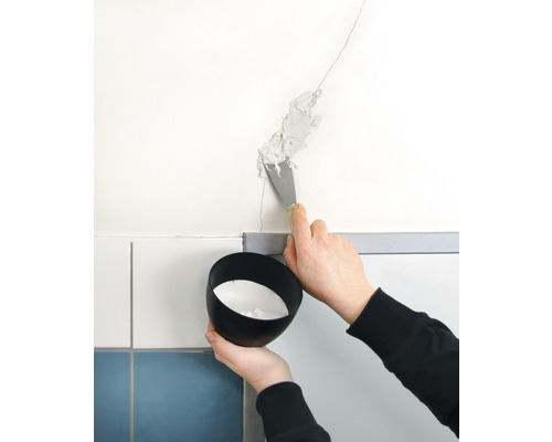 Osoba špachtlí vyplňuje trhlinu ve zdi. Drží se miska s výplňovým materiálem.