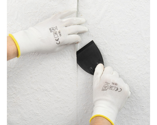 Osoba vyhlazuje tapetu špachtlí a ochrannými rukavicemi