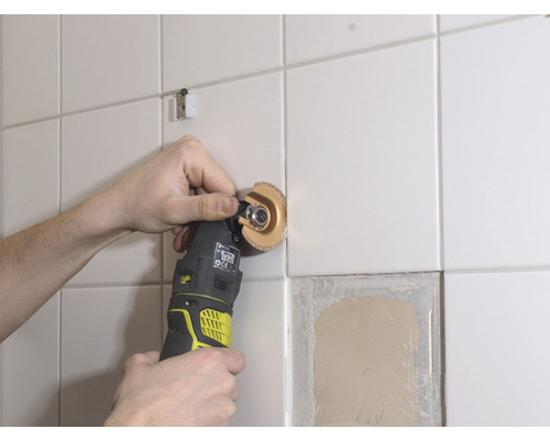 Oscilační elektrické nářadí opracovává obkládanou stěnu.