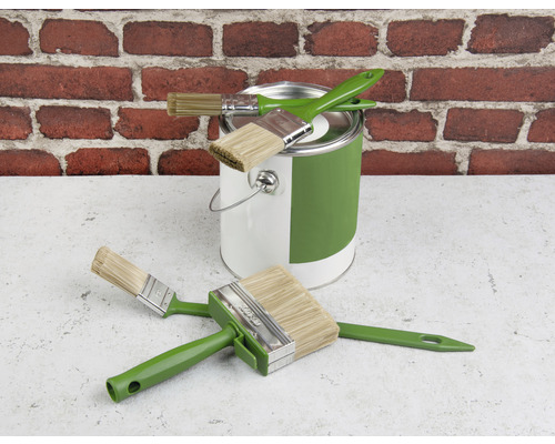 Kbelík s barvou a různé štětce před cihlovou zdí