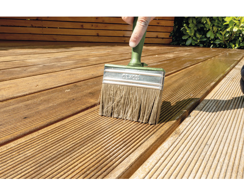 Osoba natírá dřevěnou terasu plochým štětcem.