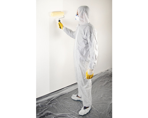 Osoba v ochranném obleku natírá válečkem zeď