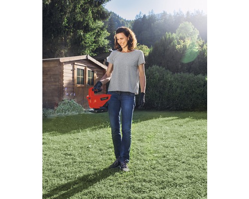 Žena používá elektrické nůžky na trávu na zahradě.