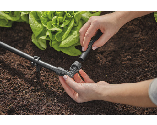 Zahradní scéna se zavlažovacím systémem a osobou připevňující spojovací kus.