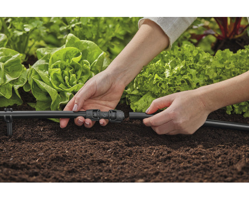 Osoba připojuje zavlažovací systém v zahradním záhonu