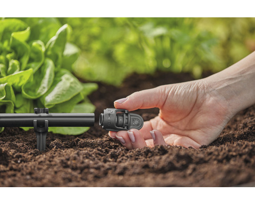 Detailní záběr osoby připevňující konektor k zavlažovacímu systému v zahradě