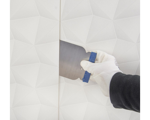 Ruka v rukavici uhlazuje tapetu hladítkem.