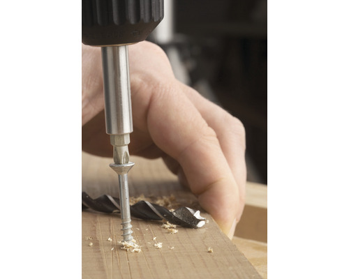 Šroub je šroubován šroubovákem do kusu dřeva.