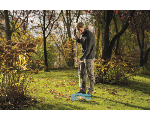 Muž shrabuje listí v zahradě hráběmi.