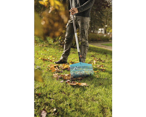 Osoba hrábě listí hráběmi na trávníku.