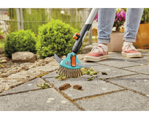 Kartáč na spáry s teleskopickou rukojetí používaný k odstraňování plevele z dlažebních kostek