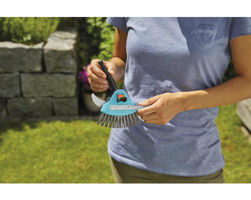 Osoba drží kartáč na spáry se škrabkou na spáry a kartáčem.