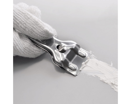 Ruka v bílé rukavici drží kovovou špachtli, která nanáší tmel na povrch.