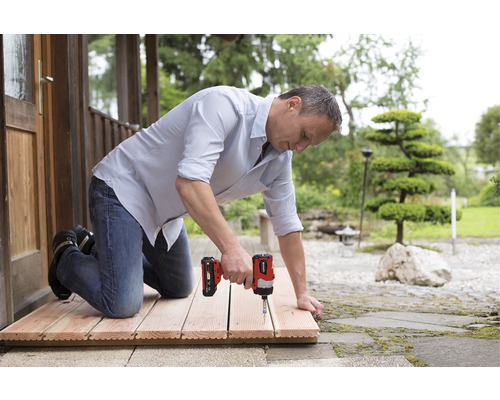 Muž montuje dřevěné dlaždice pomocí akumulátorového šroubováku venku