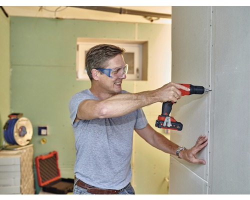 Muž šroubuje sádrokartonovou stěnu pomocí akumulátorového šroubováku