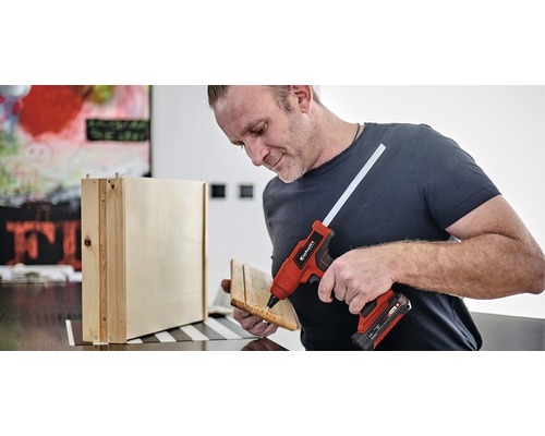 Muž používá tavnou pistoli ke spojování dřevěných dílů.