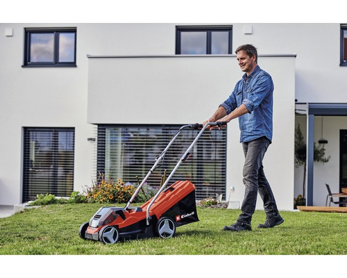 Muž používá sekačku na trávu Einhell na zahradě před domem.