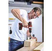 Muž vrtá akumulátorovým šroubovákem otvor do kusu dřeva.