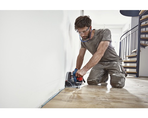 Muž řeže dřevěnou podlahu ponornou pilou.