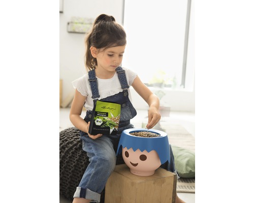 Dívka plní květináč ve tvaru obličeje semeny trávy, drží obal se semeny, bio pečeť