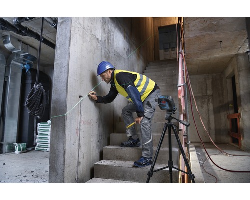 Stavební dělník pracuje s čárovým laserem na staveništi, aby označil rovnou čáru na betonové zdi.
