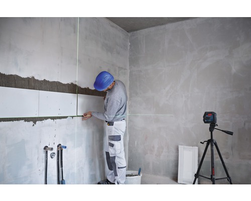 Muž pokládá dlaždice s liniovým laserem v místnosti.