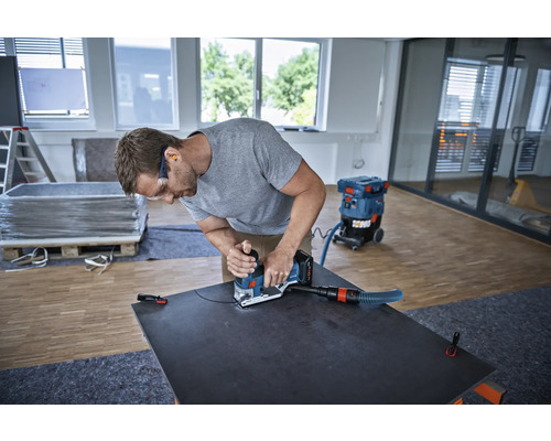 Řemeslník pracuje s drážkovací frézou na desce, vysavač je připraven.