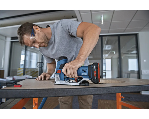 Muž používá akumulátorovou přímočarou pilu Bosch k vyřezání otvoru do dřevěné desky