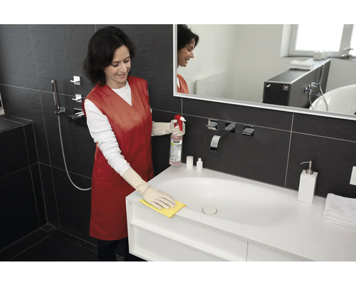 Žena čistí umyvadlo čisticím prostředkem a hadříkem v koupelně.