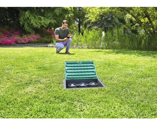 Zahrada se zavlažovacím systémem a muž s mobilním telefonem