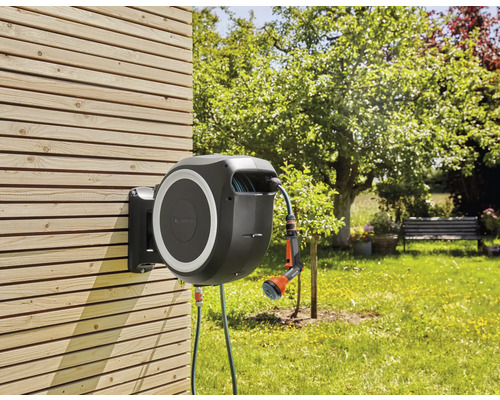 Box na zahradní hadici s hadicí a stříkací pistolí pro zavlažování zahrady, namontovaná na dřevěné stěně