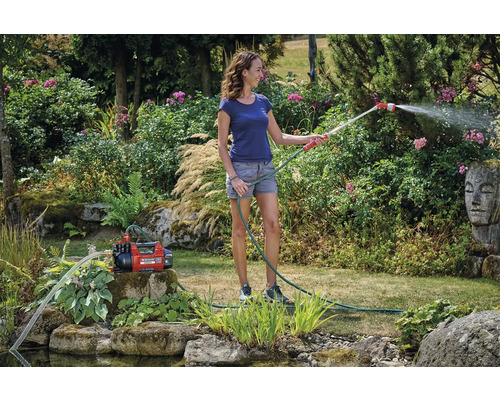 Žena zavlažuje zahradu zahradním čerpadlem a zahradní hadicí