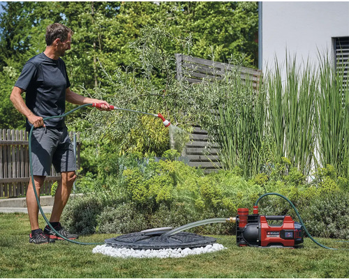 Muž zavlažuje zahradu zahradním čerpadlem a hadicí