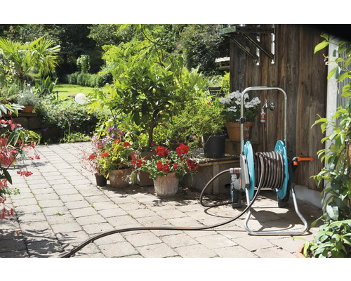 Zahradní scéna s hadicovým vozíkem, rostlinami a kamennou cestou