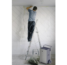 Muž na žebříku renovuje stěnu v místnosti, poblíž je odvlhčovač vzduchu