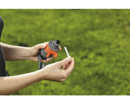 Ruce vkládají hnojivou tyčinku do zavlažovacího zařízení pro zahradu