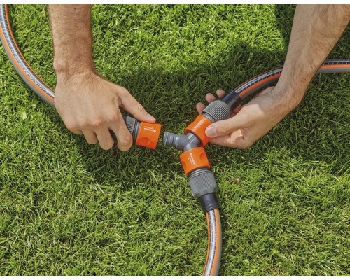 Osoba připojuje zahradní hadici k rozdělovači na trávníku