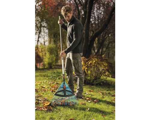 Muž hrabe listí hráběmi na listí na zahradě.