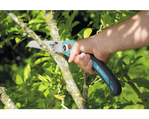 Práce na zahradě s prořezávací pilou při prořezávání větve stromu