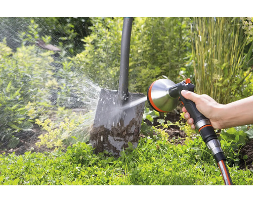 Osoba čistí špinavou lopatu pomocí postřikovače Gardena na zahradě.