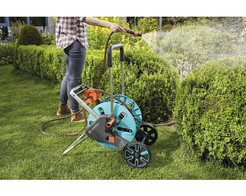 Žena zalévá zahradu pomocí vozíku na hadici a hadice