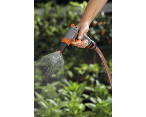 Ruka drží zahradní postřikovač, který stříká vodu.