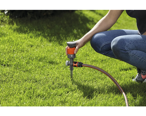 Osoba nastavuje zavlažovač trávníku na trávníku.