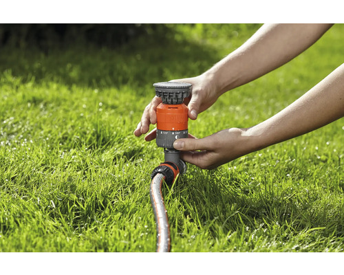 Osoba nastavuje zavlažovač trávníku na trávníku.