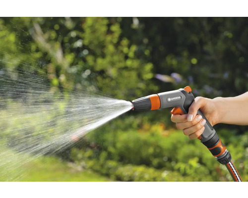 Ruka drží zahradní stříkací pistoli, ze které stříká voda.