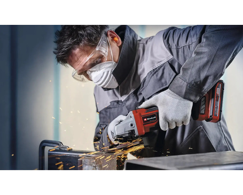 Muž brousí kov pomocí akumulátorové úhlové brusky Einhell a nosí ochranné pomůcky.