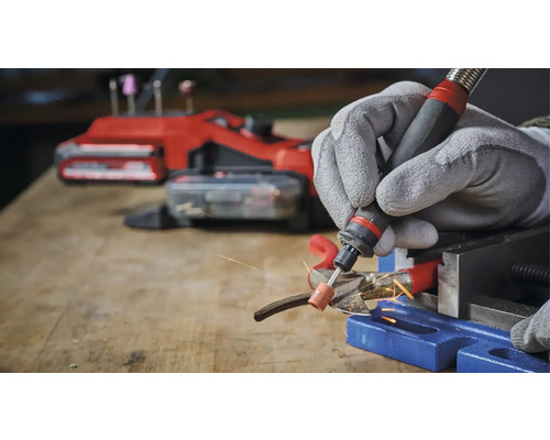 Osoba brousí kov multifunkčním nástrojem a ochrannými rukavicemi v dílně.