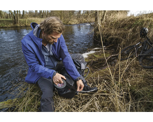 Muž s lepicí páskou na břehu řeky, vedle kola.