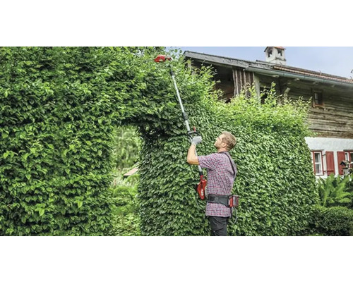 Muž stříhá živý plot pomocí akumulátorových teleskopických nůžek na živý plot