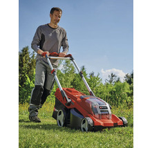 Muž tlačí červenou akumulátorovou sekačku na trávu na zahradě